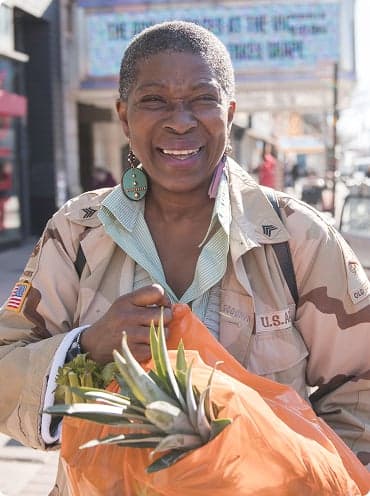 A woman carrying a bag of food and smiling at the camera