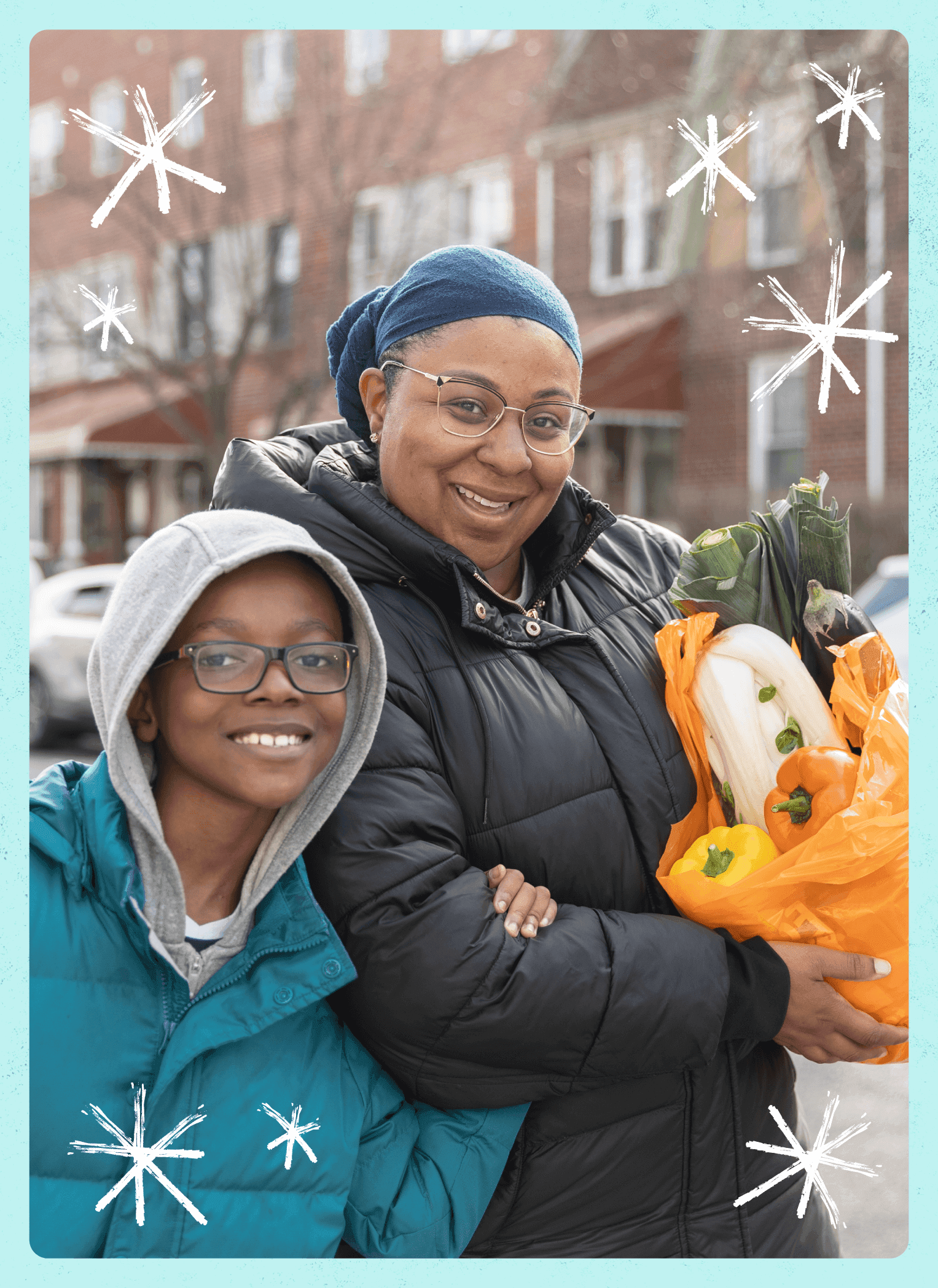 A woman holding a bag of vegetables stands next to a smiling child outdoors, both dressed in winter jackets.