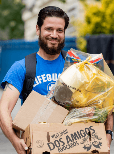 A smiling man carrying a bag of food and necessities